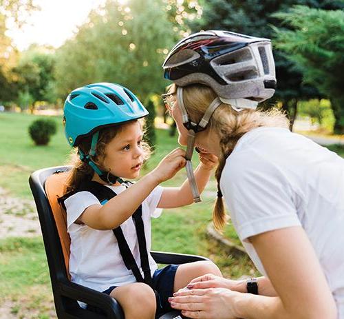 图为一个孩子坐在自行车后座上，帮妈妈系好头盔